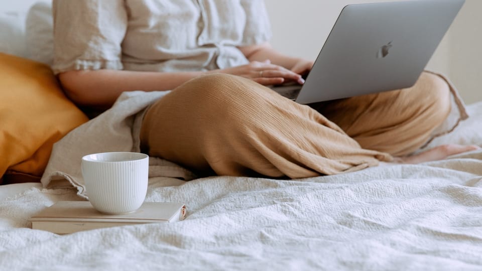 woman with coffee and laptop in bed