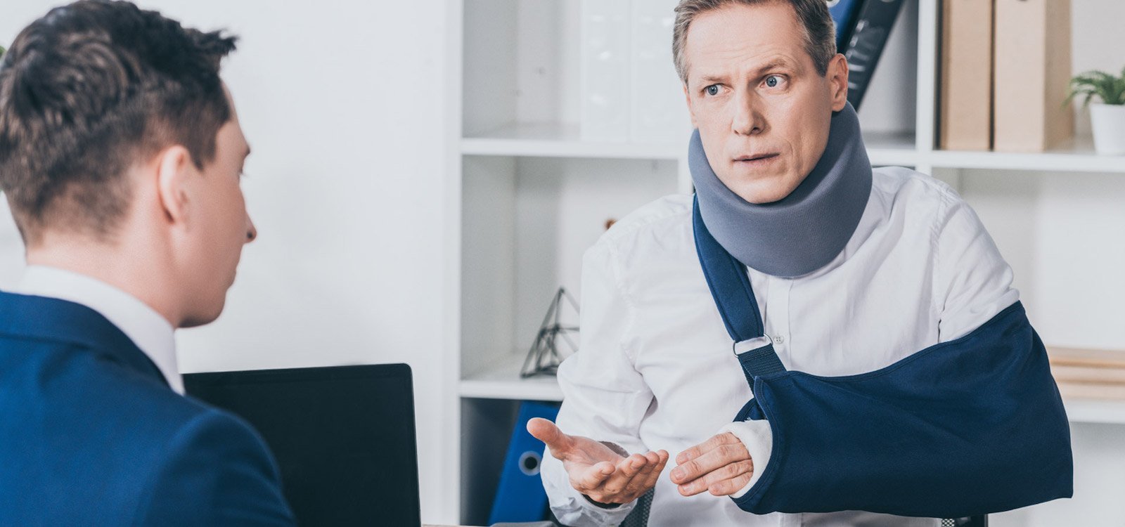 Man in neck brace and sling talking to lawyer